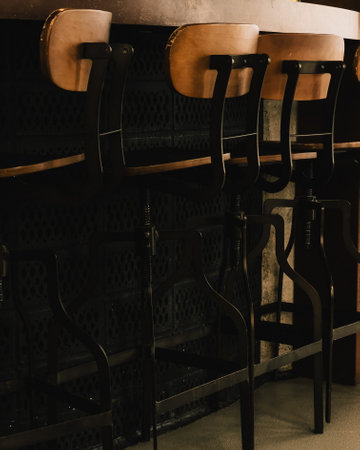 Brown vintage bar stools. Row of vintage bar stools with brown leather seats, placed in front of dark textured wall, creating nostalgic and stylish atmosphere in bar or restaurant settingの写真素材