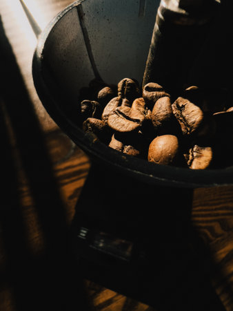 Roasted coffee beans inside coffee grinder illuminated by ray of light. Roasted coffee beans are...