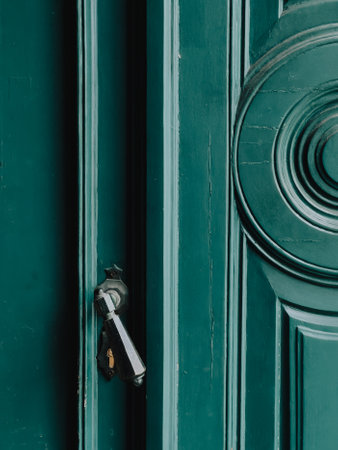 Close up view of partially opened vintage green wooden door featuring shiny metallic handle and a circular decorative element, showcasing intricate craftsmanship and timeless design. green wooden doorの写真素材
