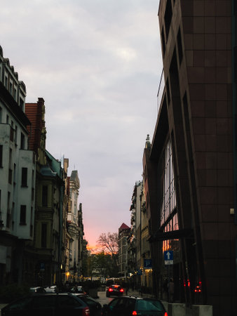 Street view at sunset with modern architecture. Wroclaw street view capturing vibrant sunset with colorful sky, showcasing modern architecture and parked cars lining road in picturesque urban settingの写真素材