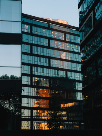 Capturing glass facade of modern office buildings, reflecting warm hues of setting sun at twilight, creates stunning urban cityscape filled with vibrant energy. office buildings and vibrant energyの写真素材