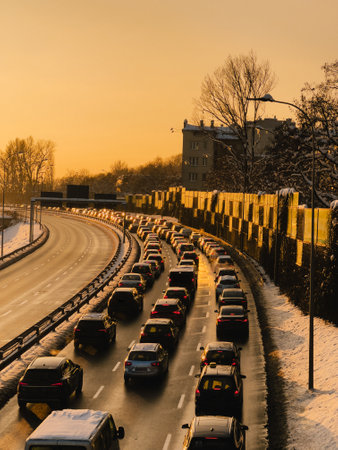 Cars stuck in heavy traffic jam on highway during sunset in winter. Many cars are stuck in heavy traffic jam on curving highway during beautiful golden sunset in winter, with snow on sides of roadの写真素材