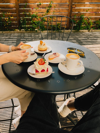 Two friends share peaceful coffee moment at outdoor cafe. Warm cafe ambiance with coffee cups and artistic pastries. inviting outdoor table, filled with sweet treats, sets mood for delightful break.の写真素材