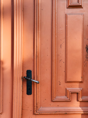 Sunlight illuminating old, weathered orange wooden door featuring classic metal handle and keyhole, showcasing texture and craftsmanship of a bygone era. Warm sunlight, weathered orange wooden doorの写真素材
