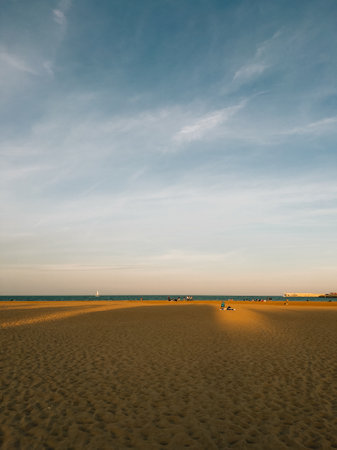 Golden sand stretching towards horizon meets a tranquil sea under vast sky filled with soft clouds, creating a serene beach scene at sunset.の写真素材
