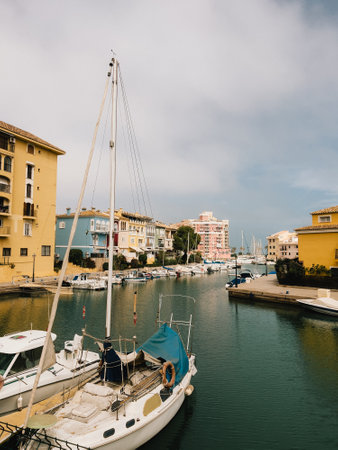 Sailboat rests in calm waters of Cabo Roig marina, surrounded by vibrant buildings, creating picturesque scene of coastal tranquility. Sailboat floating peacefully, colorful buildingsの写真素材