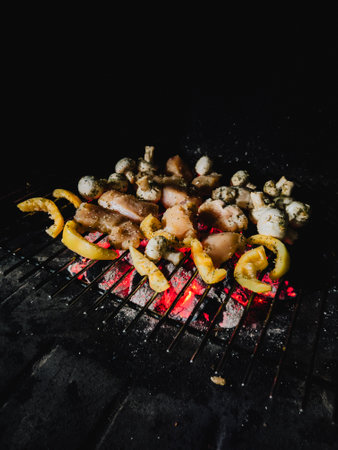 Pieces of seasoned chicken meat with sliced yellow bell peppers and mushrooms grilling on barbecue grill over glowing coals, creating delicious and smoky meal. Chicken pieces, yellow bell peppersの写真素材