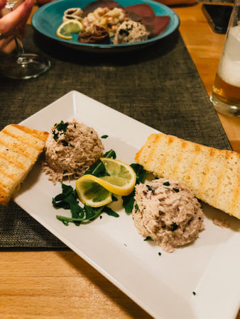 Two portions of tuna salad are served on white rectangular plate with toasted bread, lemon slices and fresh arugula, ready to be enjoyed as delicious appetizer or snack.の写真素材