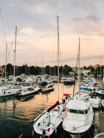 Sailboats and yachts are moored in tranquil marina as sun sets, casting warm golden glow on water and creating picturesque and serene scene of nautical beauty. Sailboats rest in marina during sunsetの写真素材