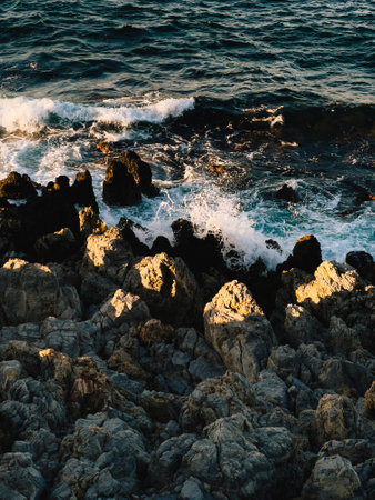 Ocean waves crashing against rugged rocky shore during sunset, showcasing stunning display of coastal power and natural beauty in tranquil, picturesque landscape. Powerful ocean waves, rocky coastlineの写真素材