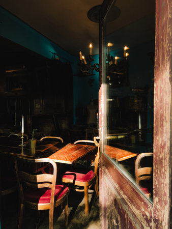 Sunlight streaming through weathered wooden door illuminates wooden tables and red upholstered chairs in cozy, vintage style restaurant, creating warm ambiance. Red chairs inside vintage restaurantの写真素材
