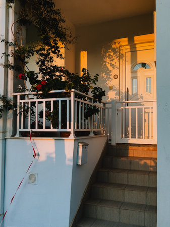 Shadows of plants dance on walls, blending with warm sunset glow. Light and texture create stunning evening composition. cozy house porch bathed in golden sunset light, casting soft shadows on wallsの写真素材