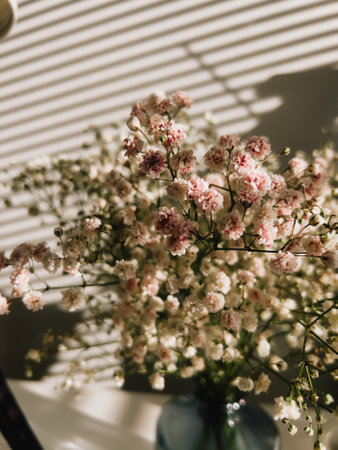Flowers in blue vase resting on table near window with blinds, casting captivating interplay of light and shadow, enhancing serene interior decor. Flowers spills from blue ceramic vaseの写真素材