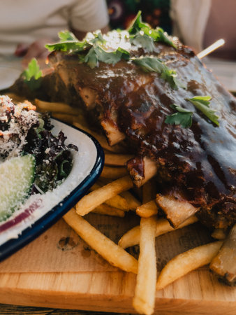 Close up of barbecue pork ribs garnished with fresh parsley, served with golden french fries and side salad, creating visually appealing and appetizing meal. Succulent barbecue pork ribs, crispy friesの写真素材