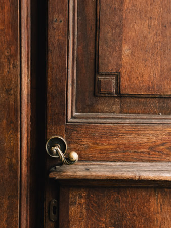 Close up of antique wooden door, showcasing brass handle with intricate carvings and rich texture of aged wood, creating sense of history and elegance. Weathered wooden door featuring brass handleの写真素材