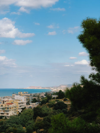 Lush green vegetation and pine trees frame picturesque view of Mediterranean coastal city with white buildings, overlooking sparkling blue sea under sky dotted with fluffy white clouds. Pine treesの写真素材