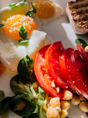 Healthy breakfast featuring fried eggs with salt and parsley, sliced tomatoes, chickpeas, fresh corn salad, and toasted bread, offering nutritious start to day. Nutritious morning meal, fried eggsの写真素材