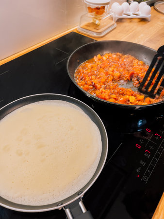 Crepe batter sizzling in pan alongside rich tomato sauce, both heating on induction hob in sleek, modern kitchen, creating delightful culinary experience. Crepe batter sizzling near tomato sauceの写真素材