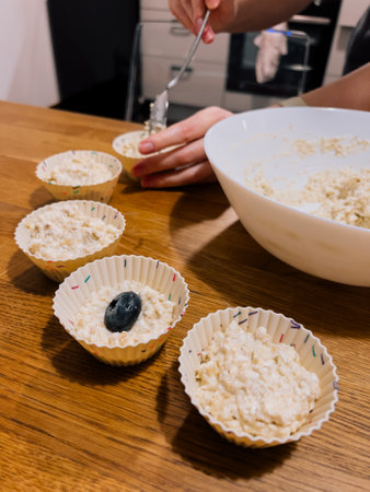 Muffin mixture scooped by hand into liners, muffin texture filled with oats and blueberries, muffin prep at home highlights healthy and cozy recipe, easy breakfast. Cupcake made of oats and fruitsの写真素材