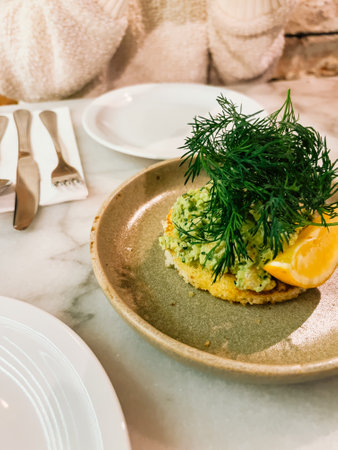 Beautifully plated fine dish with fresh dill and lemon slice sits untouched, ready to be enjoyed, while cutlery rests neatly on napkin nearby. Close-up of beautifully plated dish on marble tableの写真素材