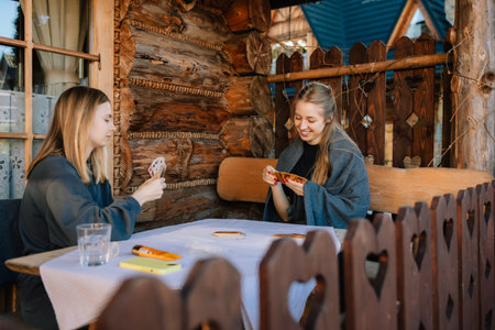 Two friends sitting at rustic wooden table on porch of cozy mountain chalet, playing cards and savoring their leisure time together in beautiful outdoors. Friends enjoying card game on mountain chaletの写真素材