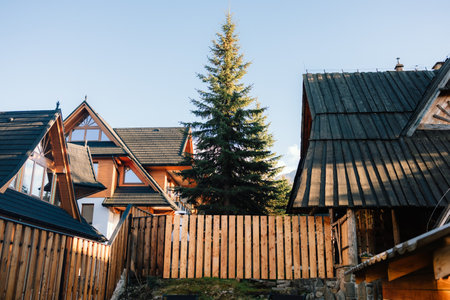 Warm sunlight illuminating wooden fence and traditional houses with tiled roofs in mountain village,...