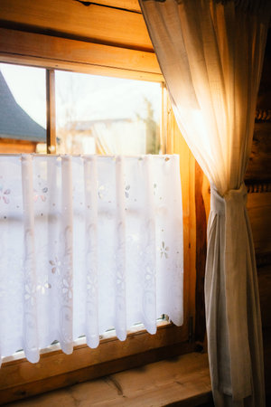 Sunlight streaming through sheer white curtains in cozy wooden cabin creates warm and inviting atmosphere, enhancing serene interior with natural light and rustic charm. Soft sunlight, wooden interiorの写真素材