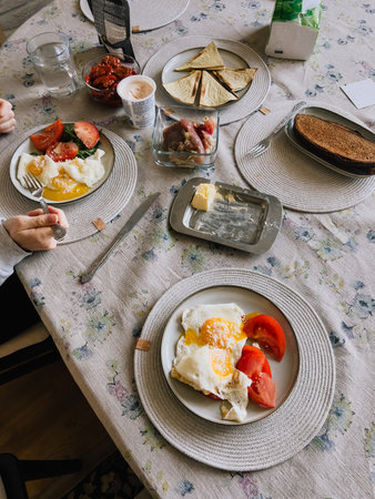 Family sharing hearty breakfast around wooden table, feasting on crispy fried eggs, ripe tomatoes,...