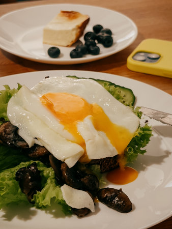Sunny side up fried egg with runny yolk is covering bed of fresh lettuce, sauteed mushrooms,...