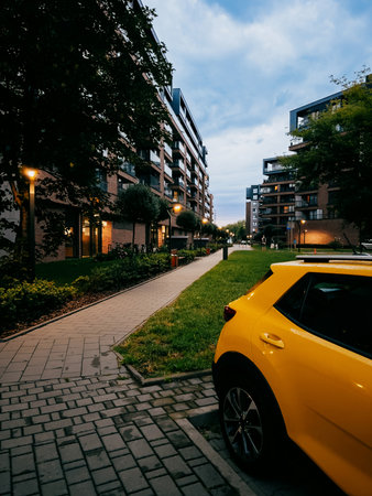 Yellow car parked on paved street, surrounded by modern residential buildings at dusk, creating tranquil and serene urban atmosphere in peaceful neighborhood. Yellow car parked in residential areaの写真素材