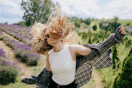 Happy young blonde woman wearing casual clothes is spinning around with open arms and hair flying in the air, enjoying freedom in a beautiful lavender field in a sunny summer day. Carefree spiritの写真素材
