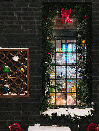 Christmas garland with red bow, baubles and dried oranges adorns window of cozy cafe during gentle...