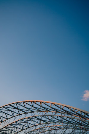 Vertical screen: curved metal beams creating robust and intricate framework rise against clear blue sky, highlighting elegance of industrial design and contemporary architecture. Modern architectureの写真素材