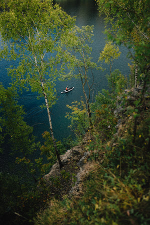 Kayaker gliding across serene lake, framed by birch trees atop cliff, embracing tranquility and...