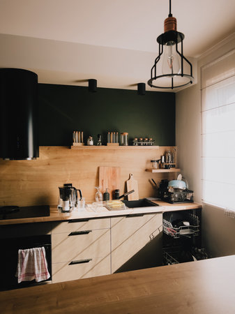 Sunlight streaming into modern kitchen featuring wooden furniture, vibrant wall, and stylish hanging lamp, crafting warm and inviting atmosphere perfect for daily living. Wooden kitchen interiorの写真素材