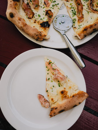 Slicing delicious pizza topped with crispy bacon on rustic wooden table, with tempting slice placed on white plate, ready for sharing. Slice of pizza with crispy bacon on white plateの写真素材