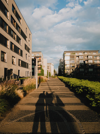 Long shadows of people walking on paved path in modern residential district with apartment...