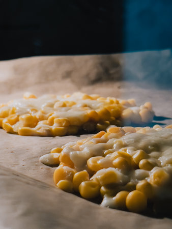 Two steaming corn fritters topped with gooey melted cheese baking on parchment paper in hot oven, filling kitchen with mouthwatering aroma that promises deliciousness. Concept of balanced nutritionの写真素材