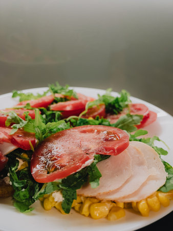 Sliced turkey breast, corn kernels, tomato slices and fresh arugula create vibrant and healthy salad on white plate, perfect for light lunch or snack. Delicious balanced meal with fresh ingredientsの写真素材
