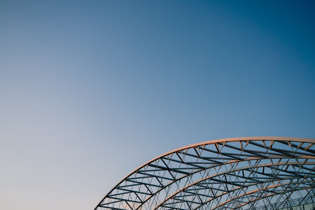 Steel beams and arches create visually appealing pattern against backdrop of vibrant blue sky, showcasing modern bridge architecture. Steel beams, design of contemporary bridge engineeringの写真素材