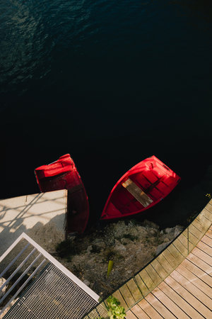 Two vibrant red boats sit near modern dock with wooden planks and concrete sections, creating...