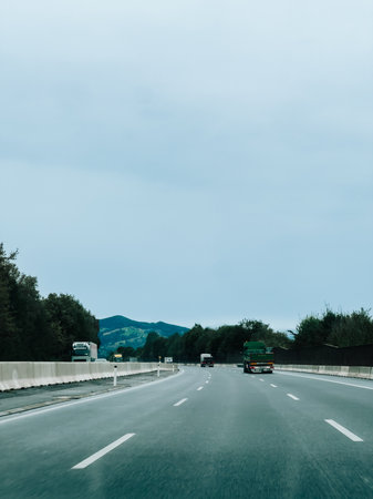 Trucks transporting goods driving on highway under cloudy sky, offering perspective of logistics and transportation in natural setting. Highway trucks hauling cargo, navigating asphalt lanesの写真素材