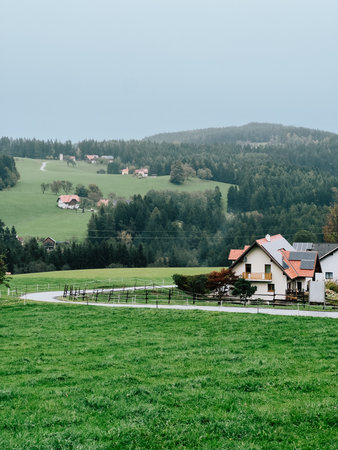 Green meadows and rolling hills create picturesque landscape, with winding road leading to traditional houses in Austrian countryside. Wooden farmhouses nestled among rolling alpine hills in Austrianの写真素材