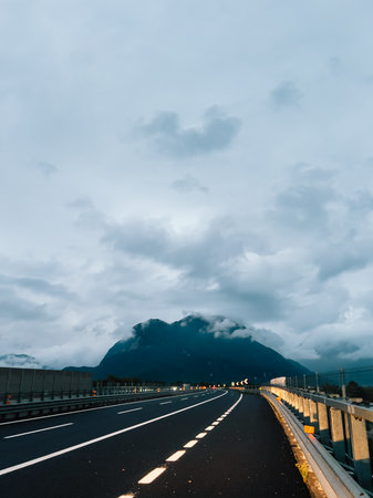 Winding highway stretching through mountain valley under cloudy sky during tranquil evening, evoking serene and peaceful atmosphere perfect for reflection and exploration. Scenic mountain backdropの写真素材