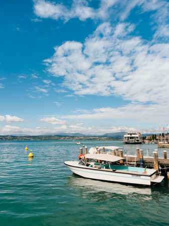 Scenic view of motorboat moored at wooden pier on Lake Garda, Italy, with mountains and blue sky in background, creating peaceful and idyllic summer scene.の写真素材