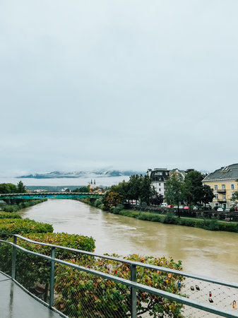 River winding through historic city, revealing colorful cityscape, arching bridge, alpine landscape with mountain under cloudy skies. River flowing through city on cloudy day with colorful bridgeの写真素材