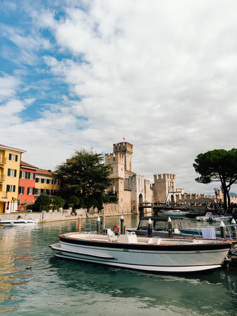 Luxury motorboat moored on Lake Garda with Scaliger Castle in background, offering picturesque view of Sirmione medieval architecture and serene lake landscape. Luxury motorboat near Scaliger Castleの写真素材