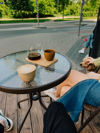 Couple sitting together at table, sipping coffee from cups and enjoying pot of freshly brewed coffee, while playful dog relaxes at their feet in charming outdoor cafe. Couple sharing coffee momentの写真素材