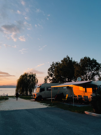 Campers parked by tranquil lake during sunset, offering serene and picturesque backdrop for unforgettable camping experience filled with relaxation and adventure. Recreational vehicles near shorelineの写真素材