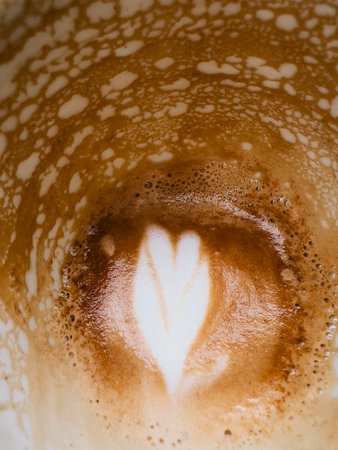 Close up of partially consumed cappuccino, showcasing fading heart shaped latte art design amidst creamy coffee foam and remnants of beverage. Heart shaped latte art fading within creamy coffee foamの写真素材